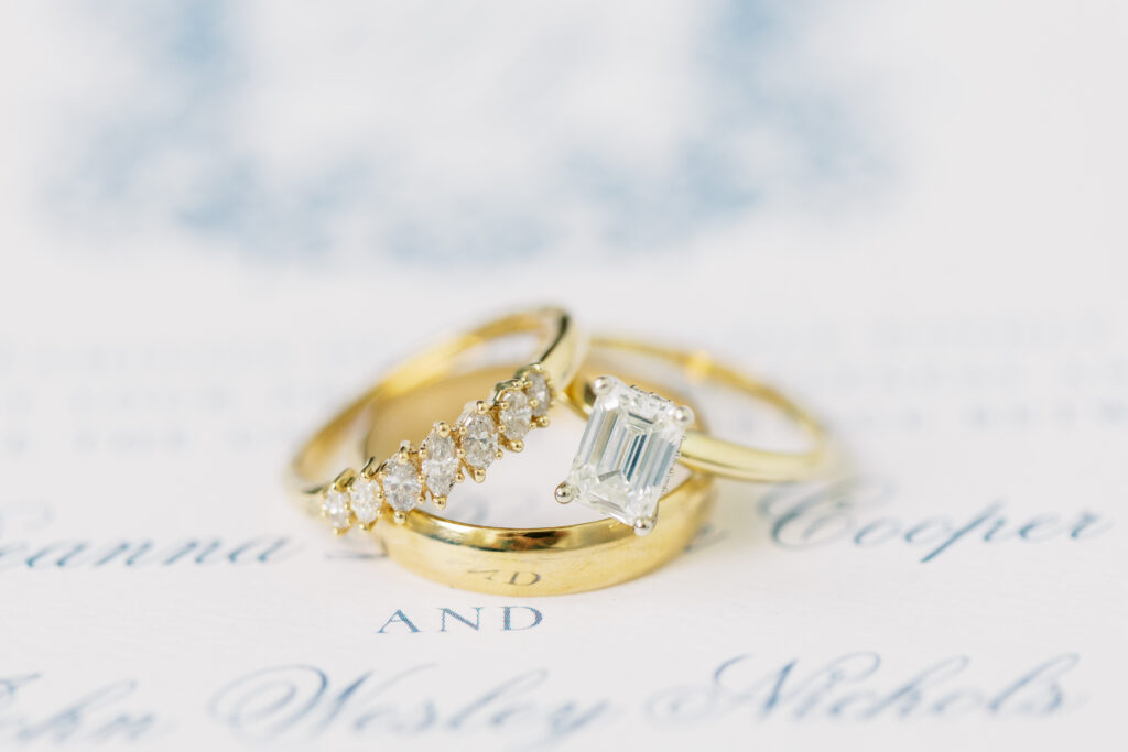 Close-up of gold wedding bands and emerald-cut engagement ring on invitation suite for Knoxville spring wedding.